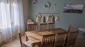 Ein Essbereich mit Holztisch und Stühlen, einem Hochstuhl, Pendelleuchten, Wandspiegeln und einem gerahmten Bild.