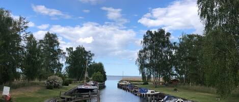 A calm waterway with boats docked on wooden piers, surrounded by grassy banks and trees.