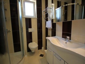 Moderni kylpyhuone, jossa on lasinen suihkuseinä, valkoinen pesuallas ja wc-istuin.