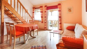 En hyggelig stue med en trætrappe, et spiseområde med et rødt borddække og en sofa med orange puder.