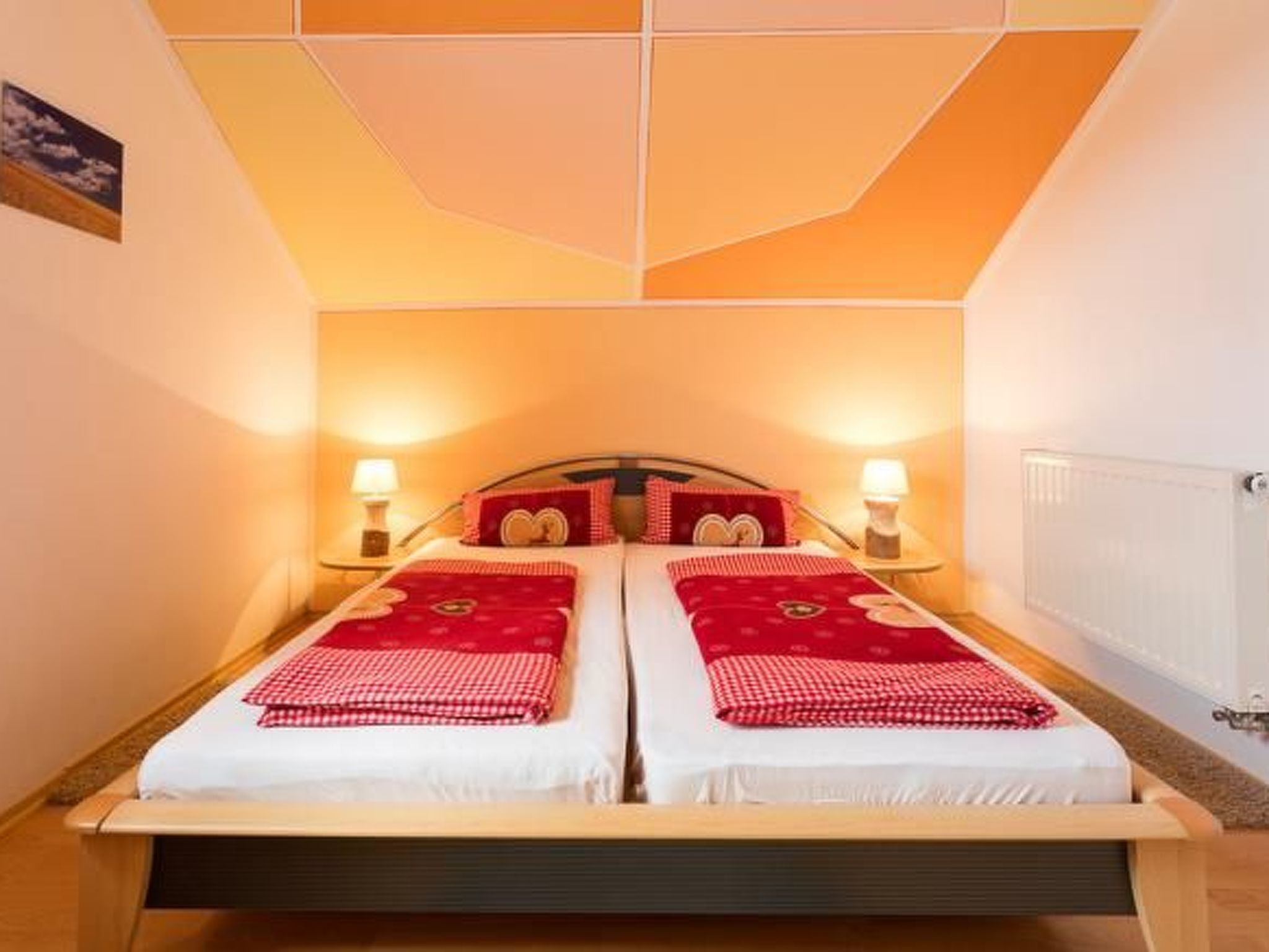 A double bed with red and white bedding, two bedside lamps, and a radiator on the wall.