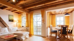 A cozy room with a wooden ceiling, a white sofa, a dining table with chairs, and a window with yellow curtains. - Am Rückerlhof -Alexi by Interhome (Geigant)