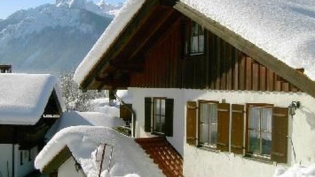 A wooden chalet with a sloped roof covered in snow, set against a mountain backdrop. - Christine by Interhome (Bischofswiesen)