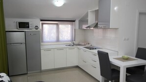 Cocina compacta con armarios blancos, microondas, refrigerador y ventana con vistas.