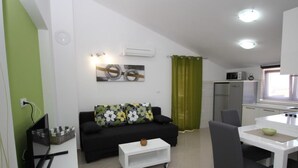 Un espacio habitable compacto con sofá, una mesa de comedor con sillas, una pequeña cocina y una cortina verde.