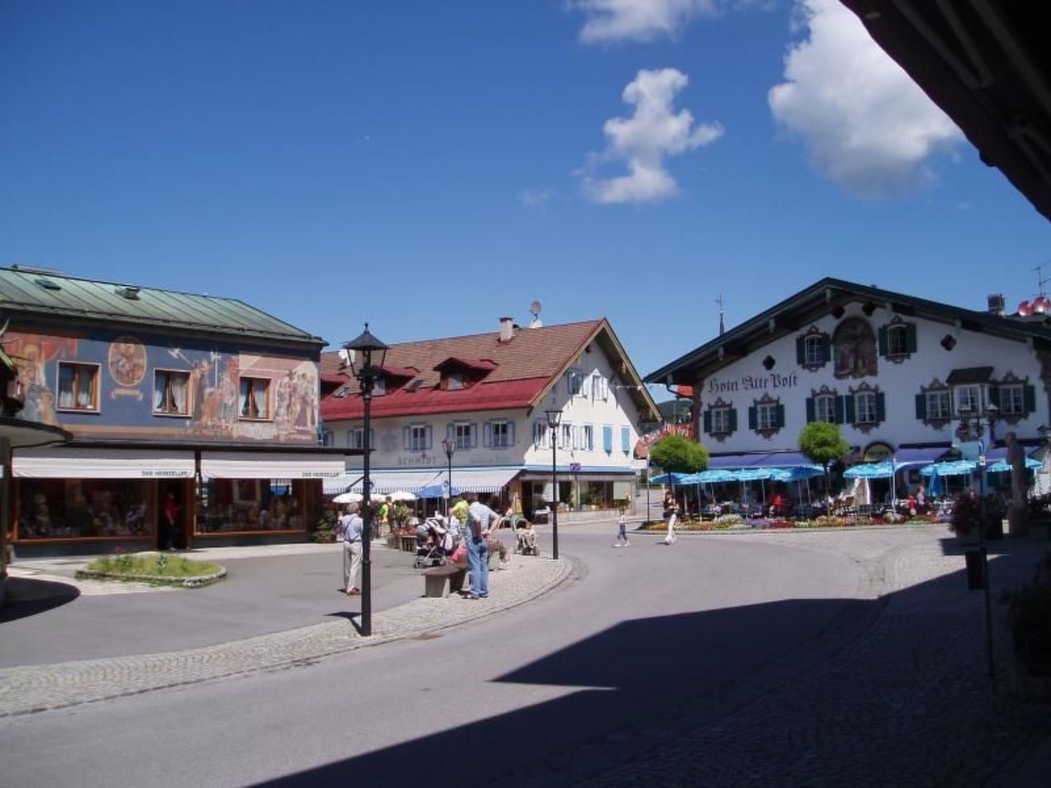 Une place de ville bordée de bâtiments traditionnels, avec des terrasses et un ciel d’un bleu éclatant.