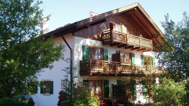 Eine zweistöckige Chalet mit Holzbalkonen, einem Garten und einem Holzzaun.