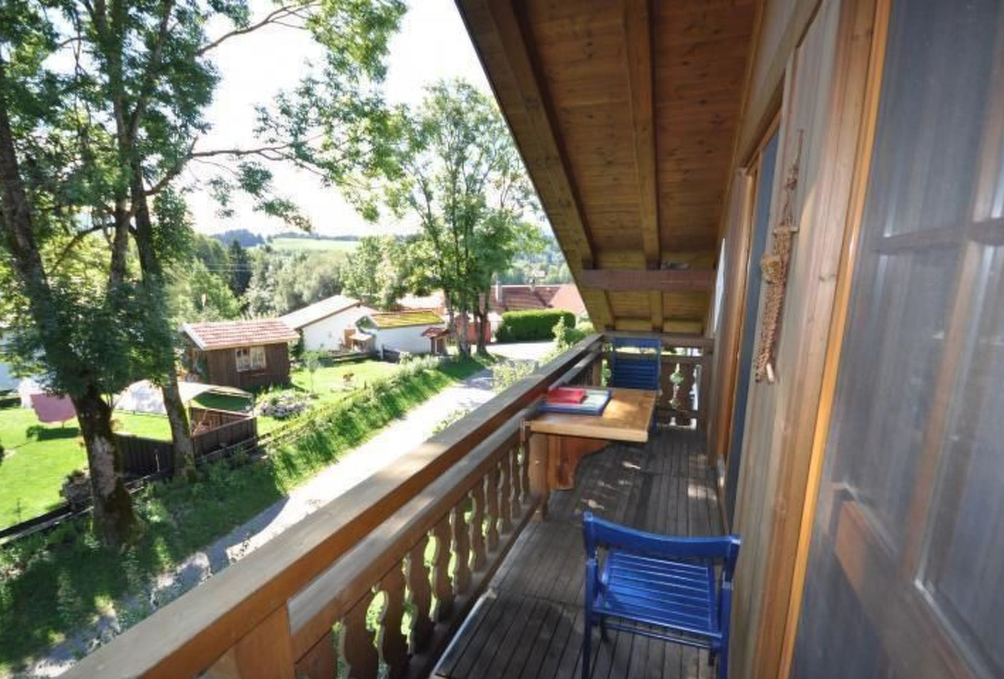 Un pontile in legno con una sedia blu, affacciato su un paesaggio verde con alberi e un piccolo edificio.