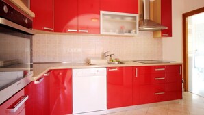 A modern kitchen with red cabinets, a stainless steel range hood, and a dishwasher. - in Baška mit Eigenem Balkon by Interhome (Krk/Baška)