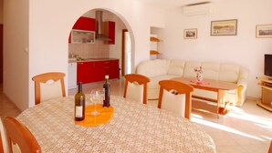 A dining area with a round table, chairs, and a bottle of wine. There is a kitchen visible through an archway. - in Baška mit Eigenem Balkon by Interhome (Krk/Baška)