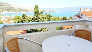 Un balcon agrémenté de fauteuils en osier et d’une table ronde, offrant une vue imprenable sur le paysage côtier, la mer et les collines lointaines.