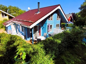 Uma casa azul com telhado vermelho, chaminé e um pequeno alpendre com móveis de exterior.