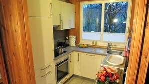 A compact kitchen with wooden cabinets, a built-in oven, a coffee maker, and a window with a view of trees. - Vacation home Sophie by Interhome (Extertal)