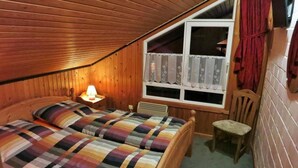 A small, cozy room with wooden walls and a sloped ceiling. There are two beds with colorful quilts, a small table with a lamp, and a window with curtains. - Vacation home Sophie by Interhome (Extertal)