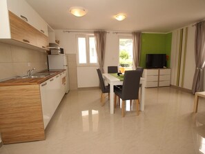 Een moderne keuken met een eethoek, een televisie en een balkon met gordijnen.