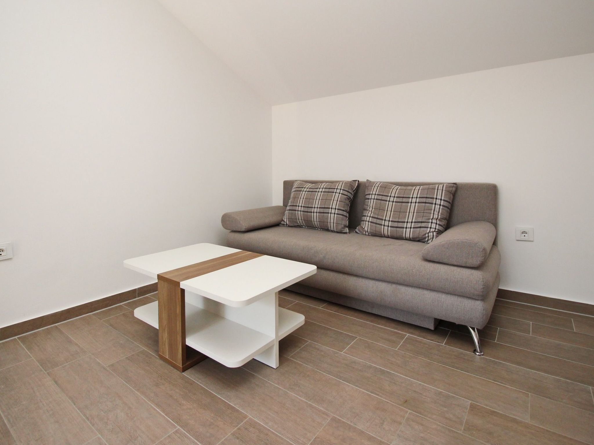 Een moderne woonkamer met een grijze bank, twee geruite kussens en een witte salontafel met houten accent.