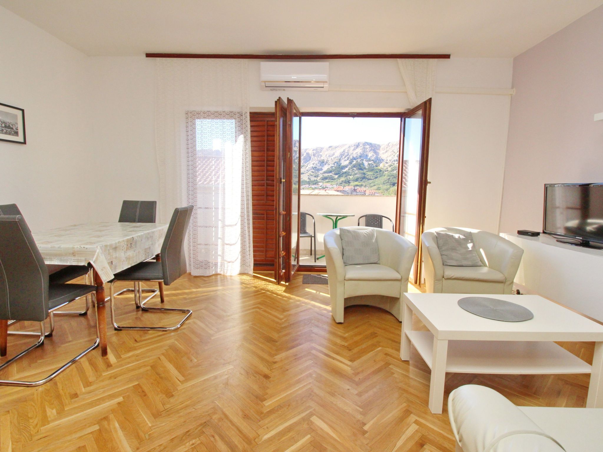 A modern living room with a dining area, a TV, and a view of mountains.