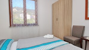 Ein Schlafzimmer mit einem Bett, einem Sessel, einem Kleiderschrank und einem Fenster mit Spitzenvorhängen.