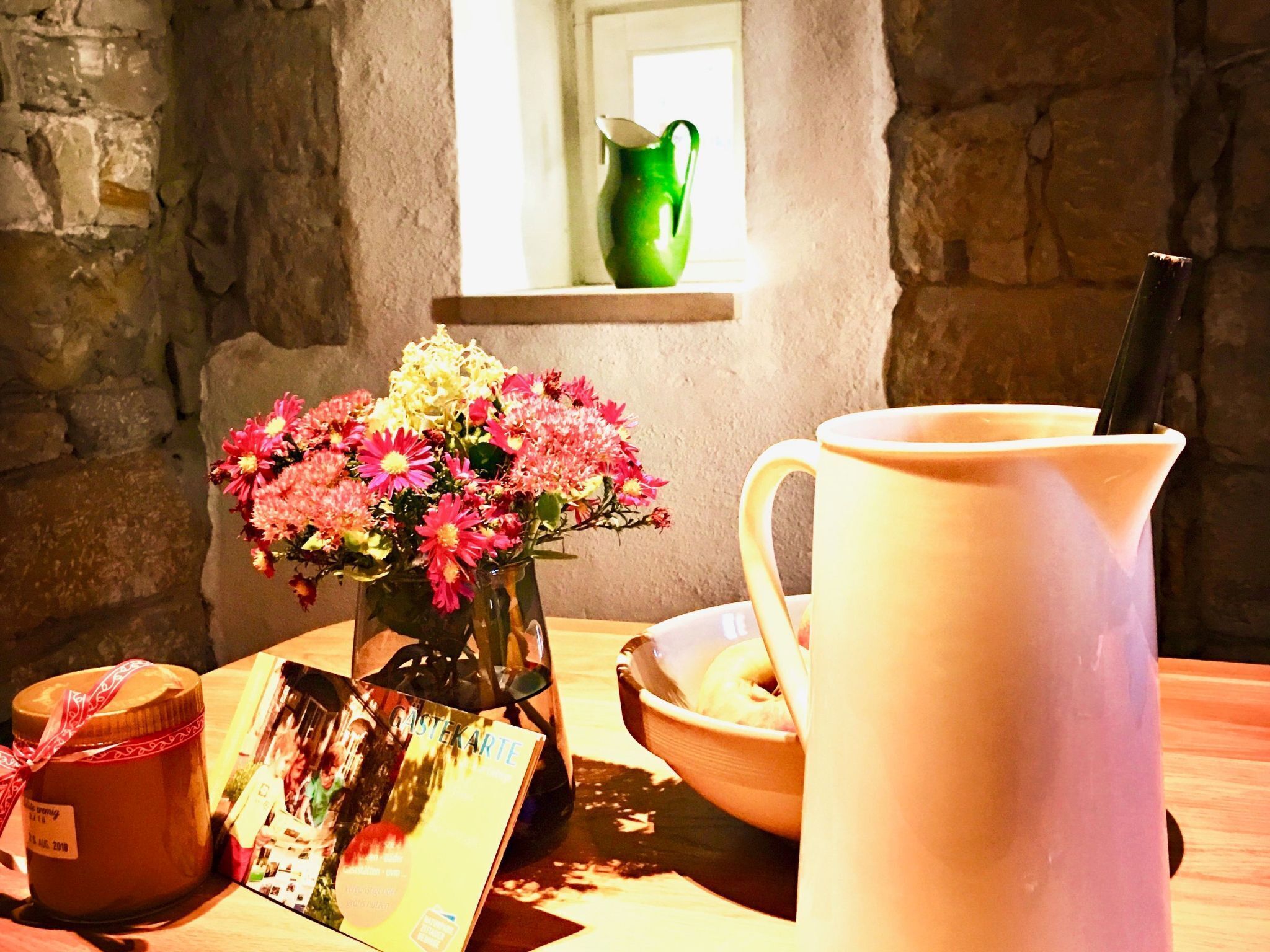 Une table avec un vase de fleurs, une bougie, un cadre photo, un pichet et un bol.