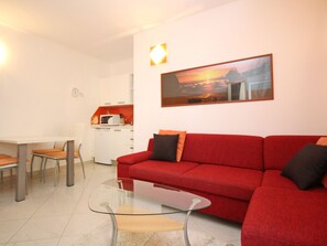 Una sala de estar moderna con un sofá rojo, una mesa de centro de vidrio y un comedor con una mesa y sillas blancas.
