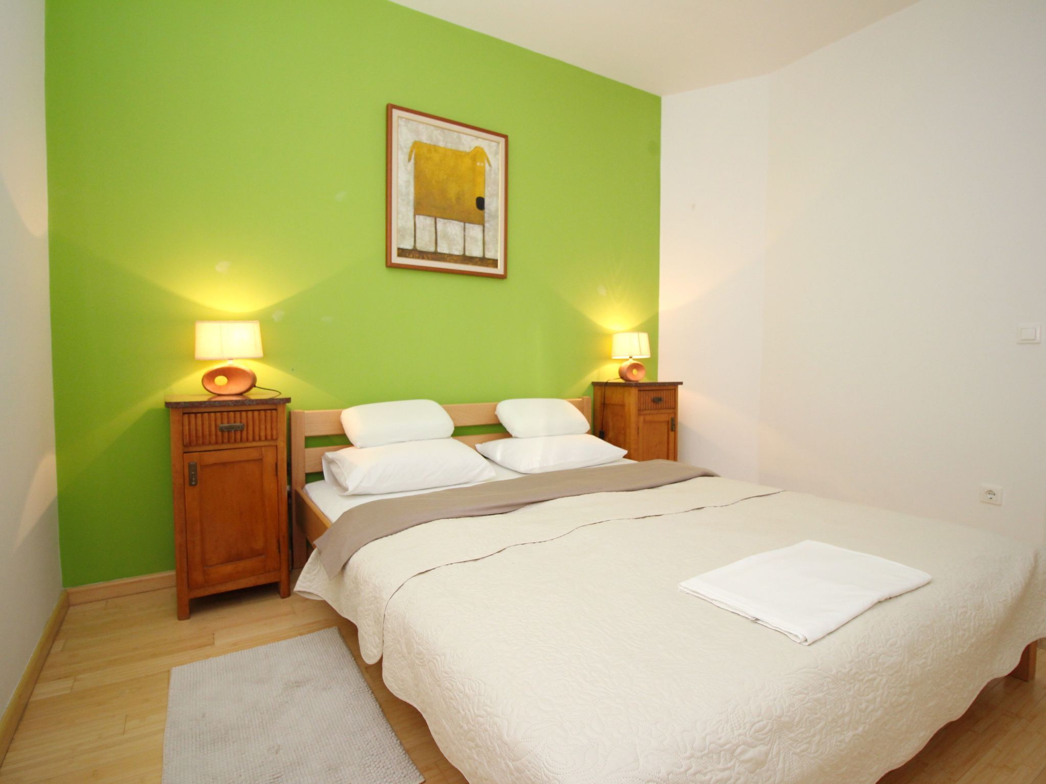 A bedroom with a bed, two bedside tables with lamps, a wooden headboard, and a green wall.
