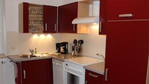 Una cocina compacta con armarios rojos, un lavavajillas blanco y un horno empotrado.