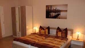 Una cama doble con una manta a rayas, dos mesitas de noche con lámparas, un armario y un cuadro de un muelle en la pared.