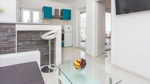 Una cucina moderna con mobili color petrolio, uno schienale in pietra e un tavolo da pranzo in vetro con della frutta.
