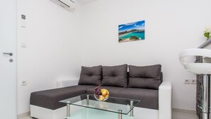 Un soggiorno moderno con un divano angolare grigio, un tavolino in vetro con della frutta e un quadro raffigurante una spiaggia.