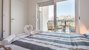 Una camera d'albergo con un letto, un balcone con tavolo e sedie e vista sulle montagne.