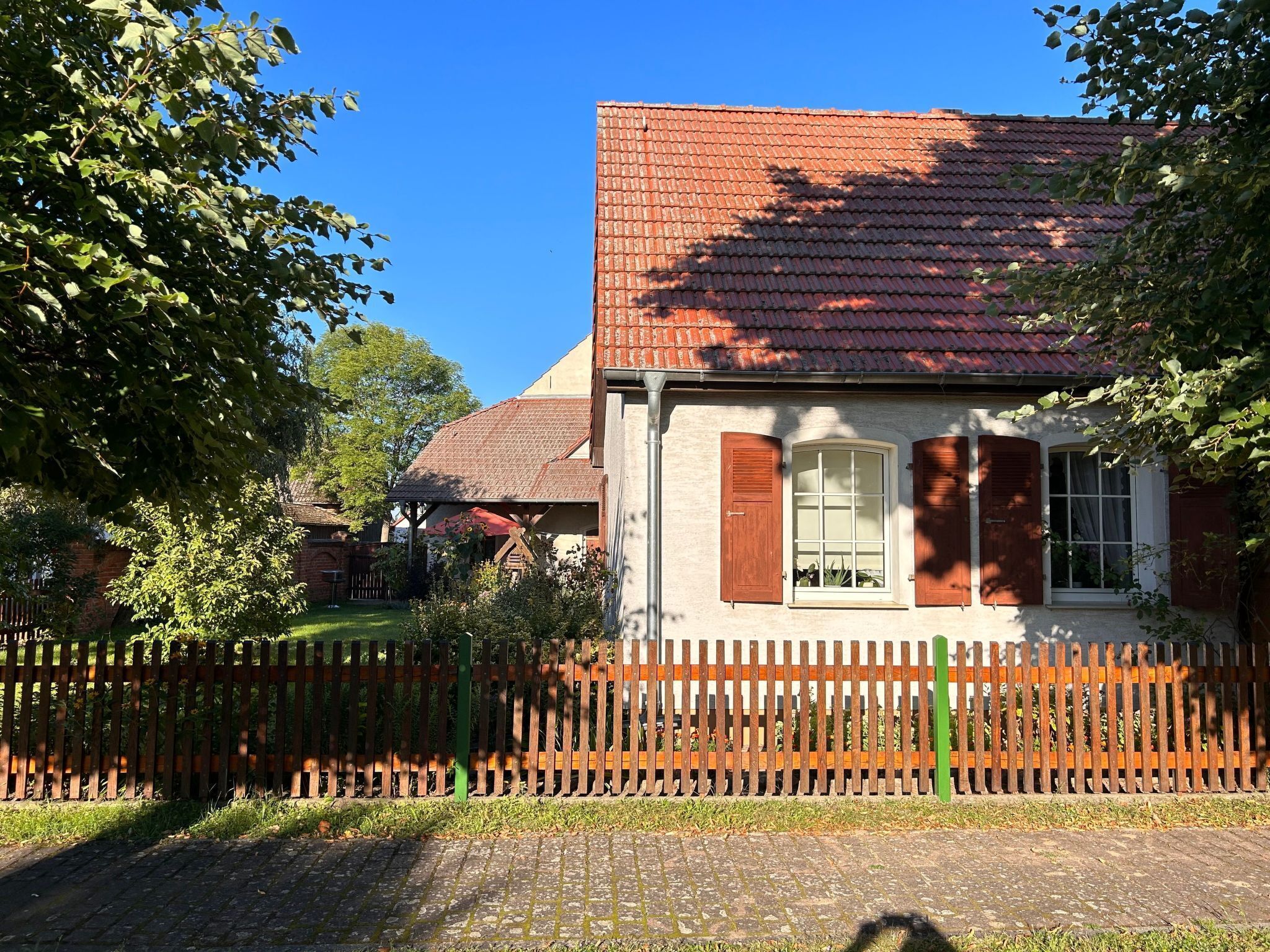 Ett hus med ett rött tegeltak, ett trästaket och en trädgård.
