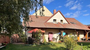 A two-story house with a red-tiled roof, a covered porch, and a small garden area with a bench and potted plants.
