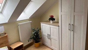 A room with a sloped ceiling, skylights, a radiator, a potted plant, a wooden cabinet, and a small wooden table.