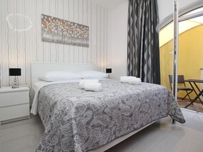 Quarto de hotel moderno com uma cama grande, duas mesas de cabeceira com abajures, uma janela ampla com vista e uma parede com padrão.