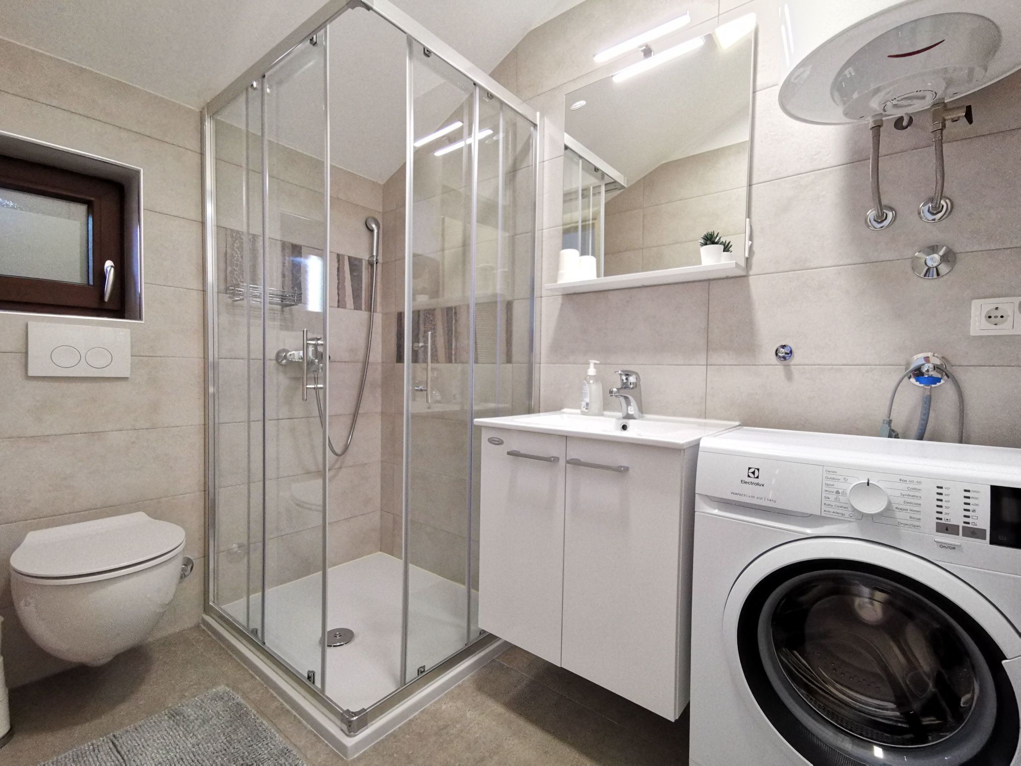 Un baño moderno con ducha de vidrio, inodoro, lavabo y lavadora.