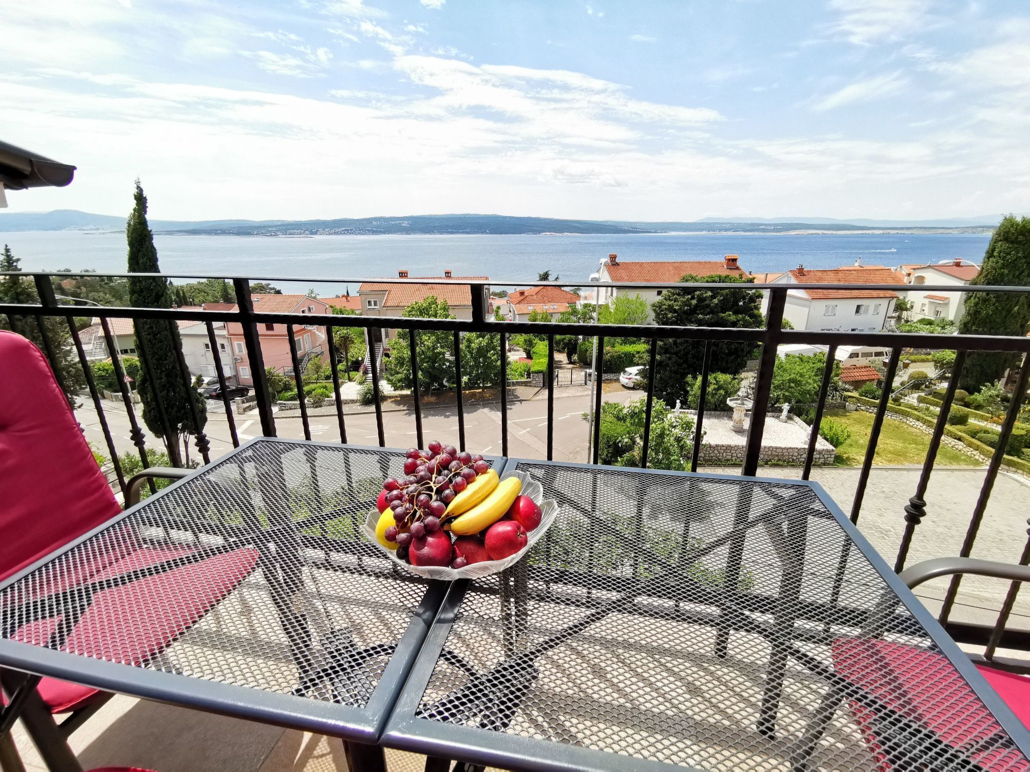 Ein Balkon mit Tisch, gedeckt mit Obst, mit Blick auf eine Küstenstadt und das Meer.