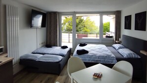 A hotel room with two beds, a TV, a table, and a view of greenery outside. - Appartement in Sankt Englmar mit Großem Balkon by Interhome (Sankt Englmar)
