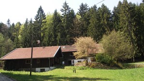 Una casa de madera con techo de tejas, rodeada de césped y un bosque denso.