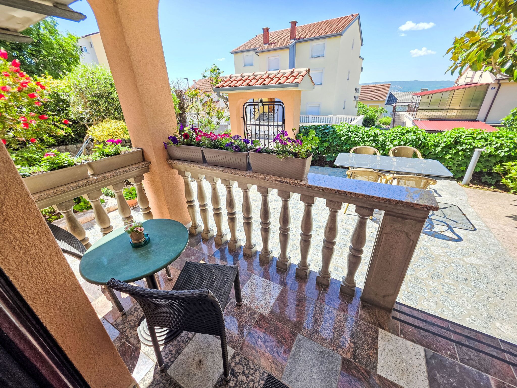 Un balcone con tavolo e sedie, piante in vaso e vista su un edificio con tetto in tegole.