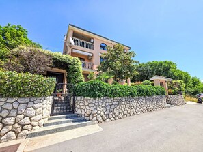 Ein mehrstöckiges Gebäude mit einer steinernen Eingangsmauer, einem Balkon und blauem Himmel.