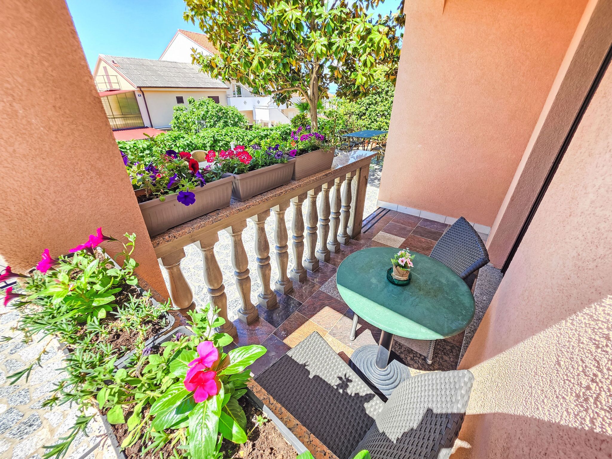 Un balcon avec une table et des chaises vertes, des plantes en pot et une vue sur les bâtiments environnants.