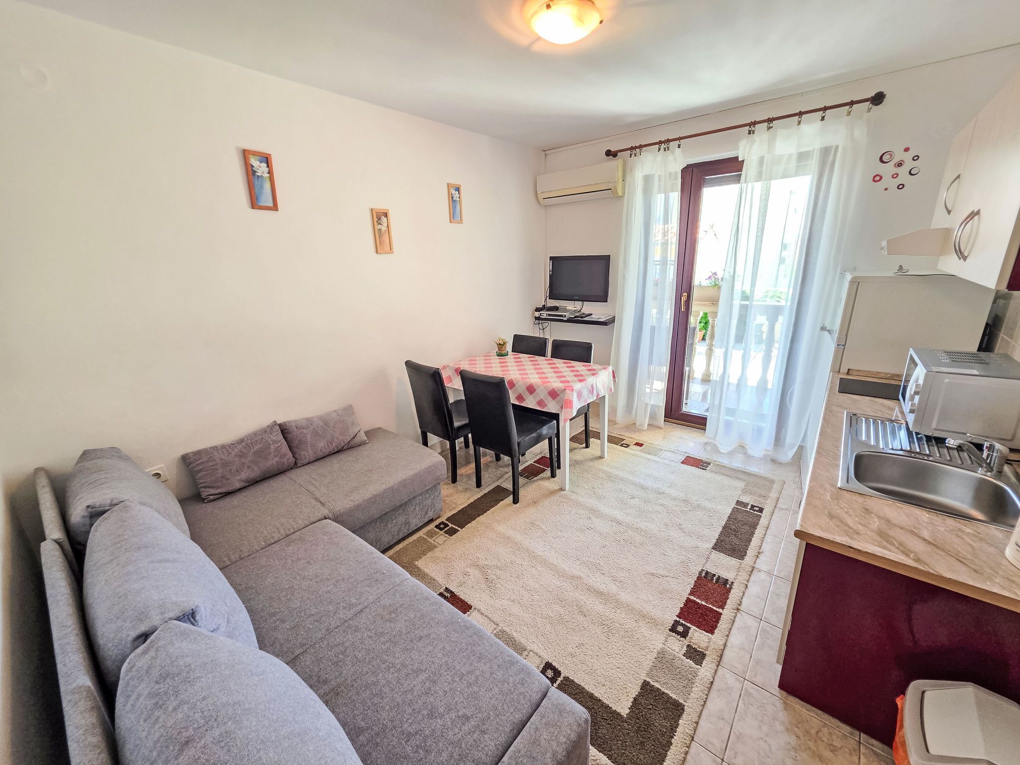 A living room with a sofa, a dining table with chairs, a TV, and a kitchen area with a sink and a microwave.