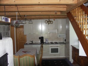 Una cocina compacta con vigas de madera, una mesa de comedor con sillas y un horno empotrado.