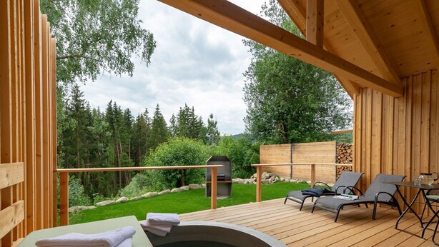 Una terraza de madera con jacuzzi, sillones de descanso y una parrilla.