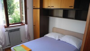 Une chambre à coucher avec un lit, des placards en bois au-dessus, une fenêtre avec des rideaux et un radiateur en dessous.
