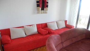 Un canapé rouge avec des coussins blancs, dans une pièce dont le sol est recouvert de parquet en chevrons.