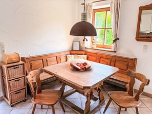 Une table à manger en bois, des chaises, un banc, des paniers en osier et une fenêtre avec des rideaux.