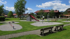 Une aire de jeux avec un toboggan rouge, des balançoires et une structure d’escalade.