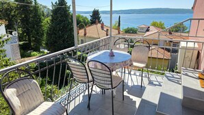 Ein Balkon mit Tisch und Stühlen mit Blick auf einen See, umgeben von Grünflächen und Gebäuden.