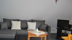 A modern living room with a grey sofa, a wooden coffee table, a television, and a small table with a white vase. - Fewo Stricker 23 by Interhome (Walkenried)